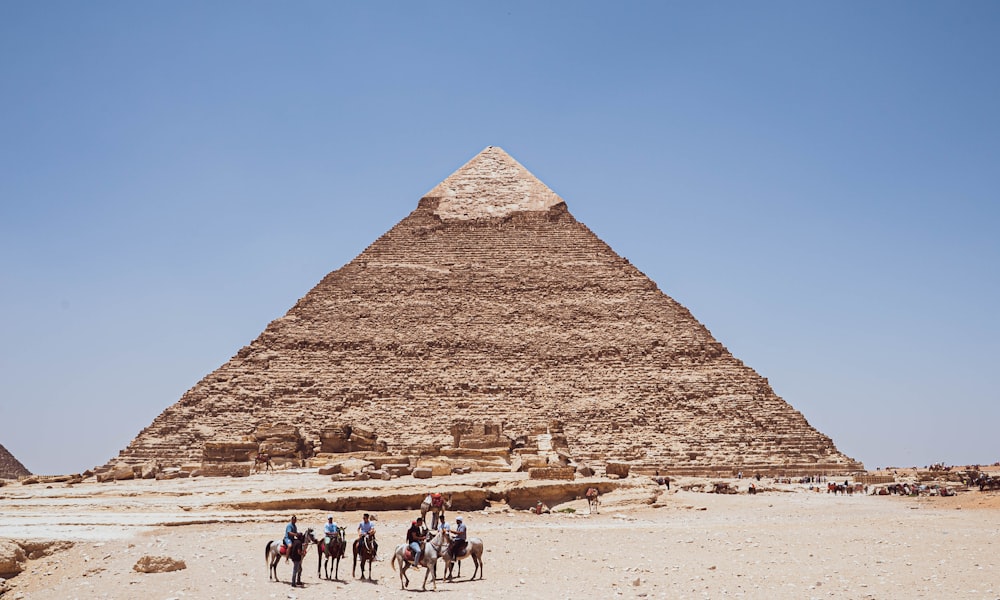 a group of people riding camels in front of a pyramid