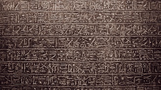 Intricately carved ancient hieroglyphics cover the surface of a stone tablet. The symbols and characters are arranged in horizontal lines, showcasing detailed craftsmanship and artistry.