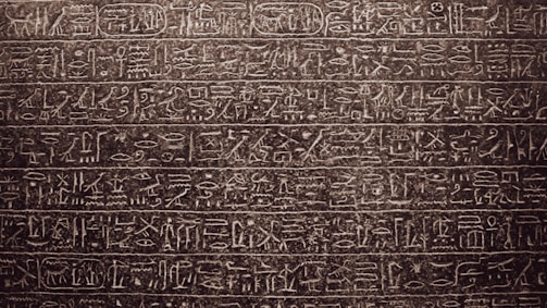 Intricately carved ancient hieroglyphics cover the surface of a stone tablet. The symbols and characters are arranged in horizontal lines, showcasing detailed craftsmanship and artistry.