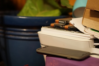 A compact phomemo printer resting on a cluttered desk next to journals, labels, and colorful pens.