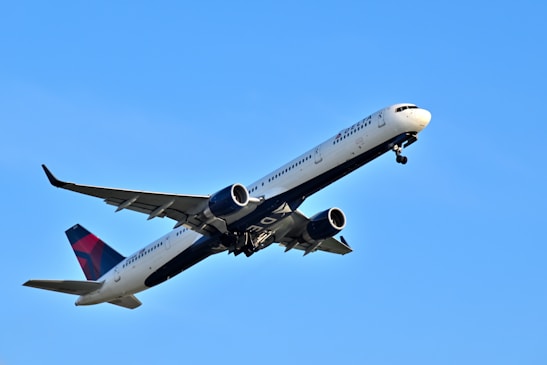 A sleek modern airplane ascending into a bright blue sky during sunrise.
