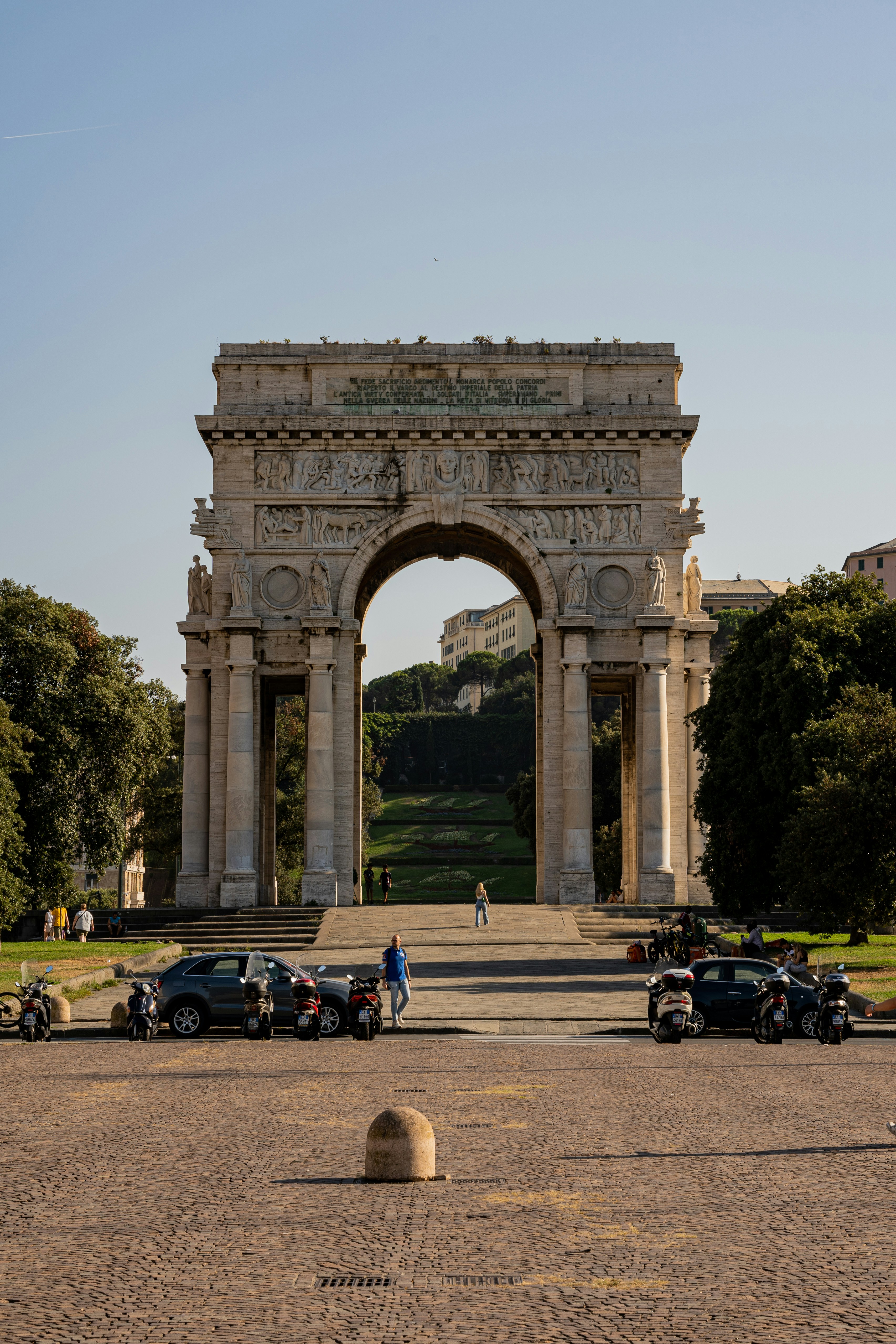 a large stone archway with cars parked in front of it with Arc de Triomphe in the background