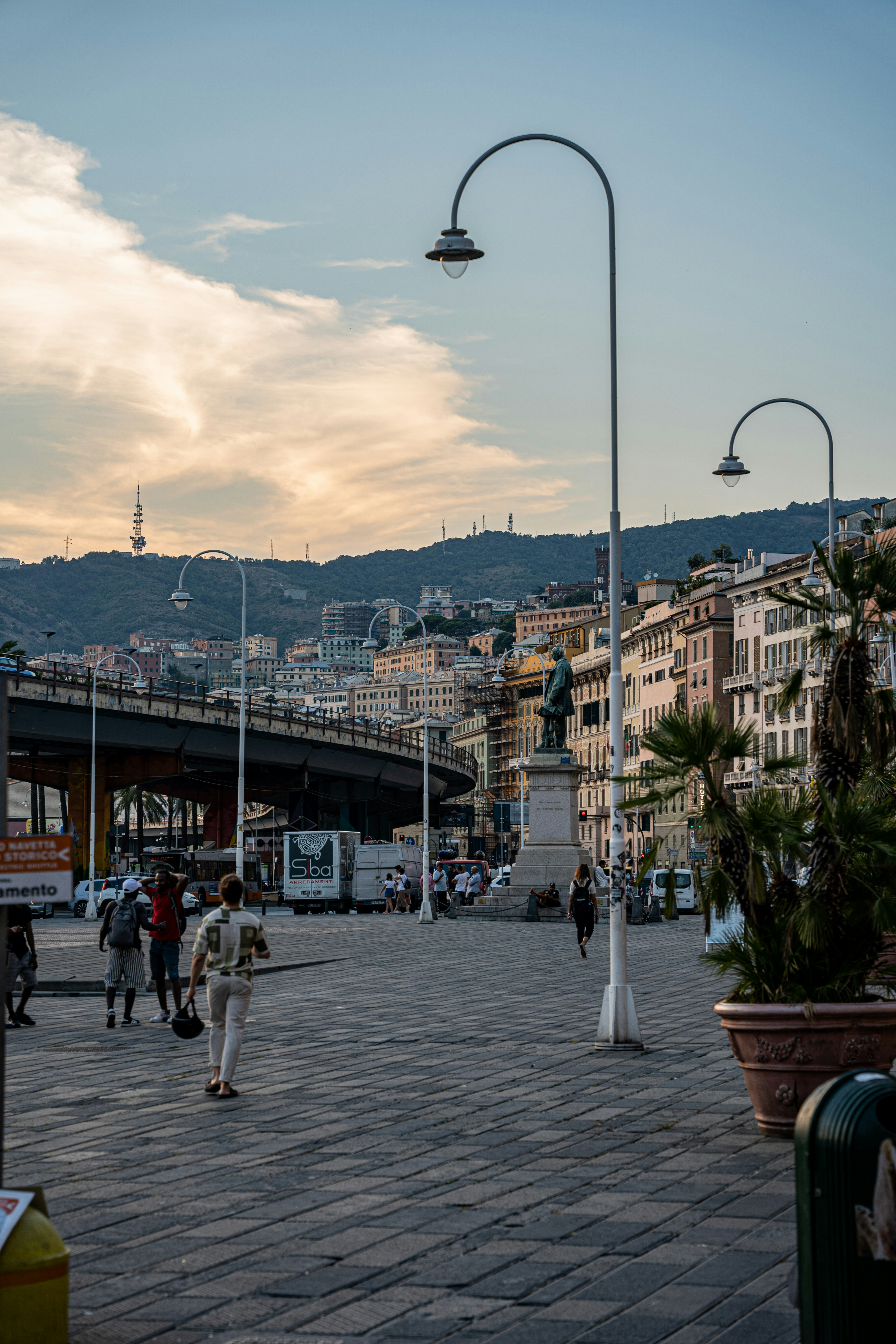 a group of people walking on a stone path with a bridge and buildings in the background