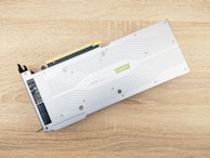 A graphics card is placed on a wooden surface with a minimalist design featuring a metallic silver finish. Engraved details include the text 'RTX 2080 SUPER' with an accented green 'super' logo. Visible are connector ports and screws, indicating parts of the card's functional design.