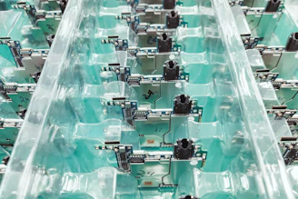 A collection of electronic circuit boards organized neatly in transparent plastic trays. The boards are lined in rows, displaying components, connectors, and intricate circuitry on a teal background.