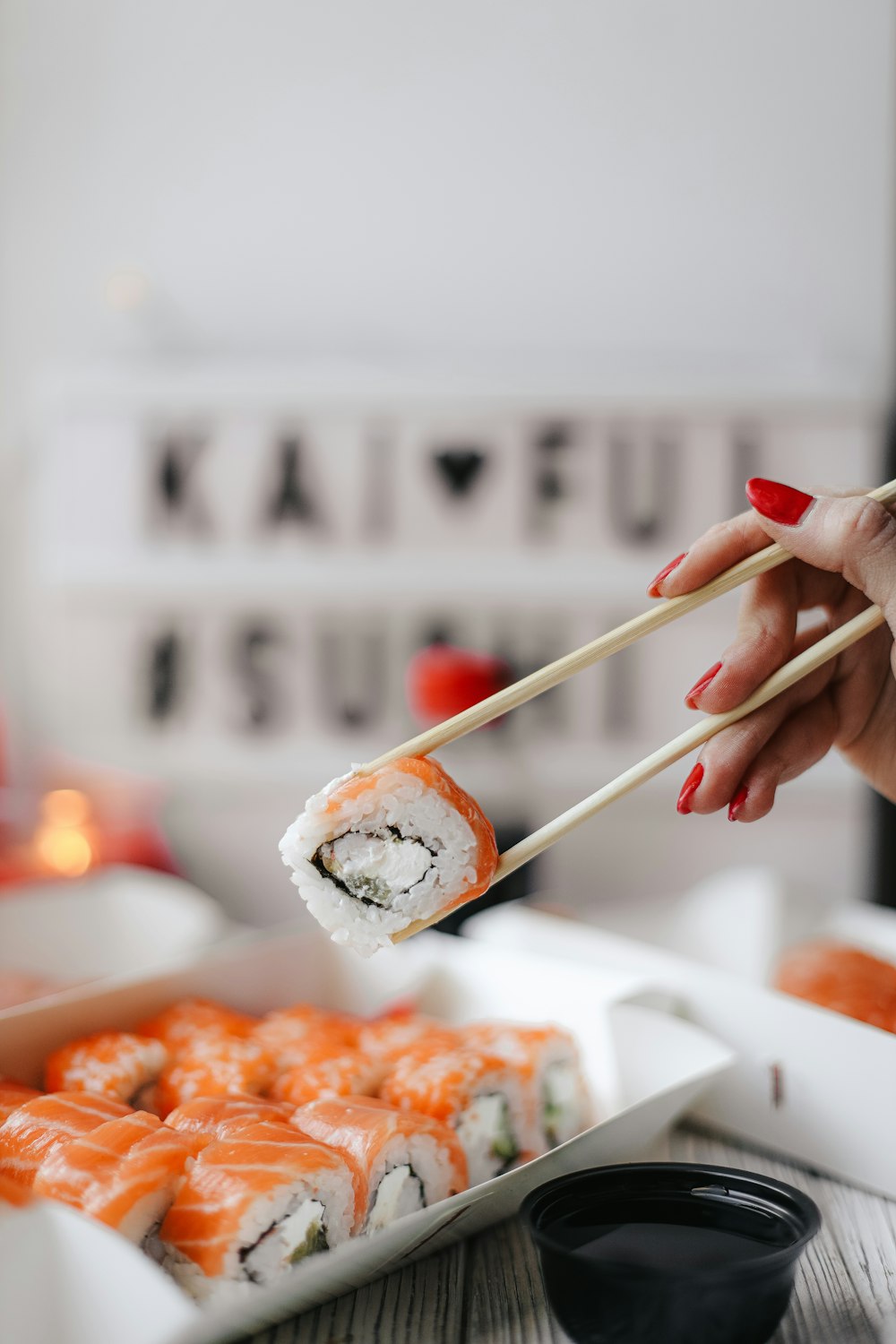 a hand holding chopsticks over a plate of sushi