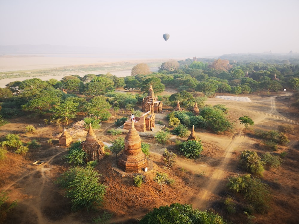 a hot air balloon flying over a landscape with trees and buildings