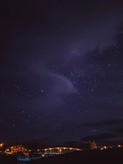 A serene night sky filled with twinkling stars over a quiet bridge.