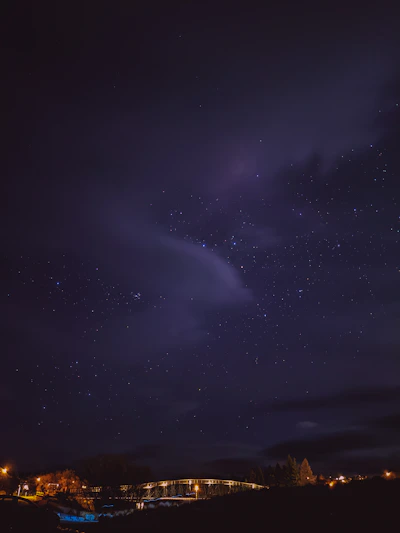 A serene night sky filled with twinkling stars over a quiet bridge.