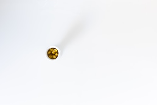 A small white container containing yellow capsules, possibly dietary supplements or medication, positioned on a smooth, white surface.