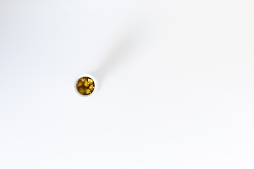 A small white container containing yellow capsules, possibly dietary supplements or medication, positioned on a smooth, white surface.