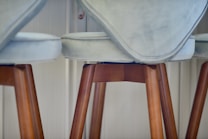 A close-up view of cushioned bar stools with light grey upholstery and wooden legs, set against a softly lit interior background.
