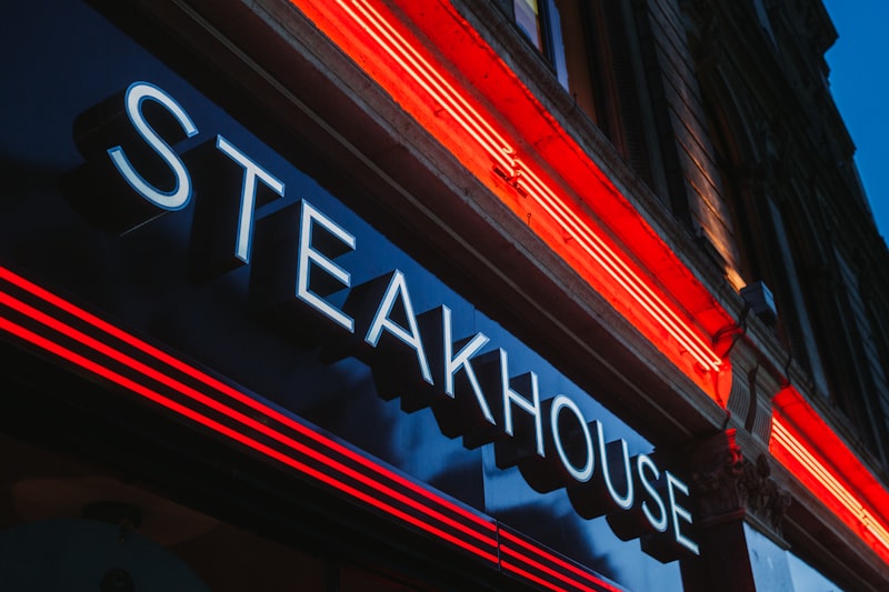 Illuminated STEAKHOUSE neon sign on a building at dusk