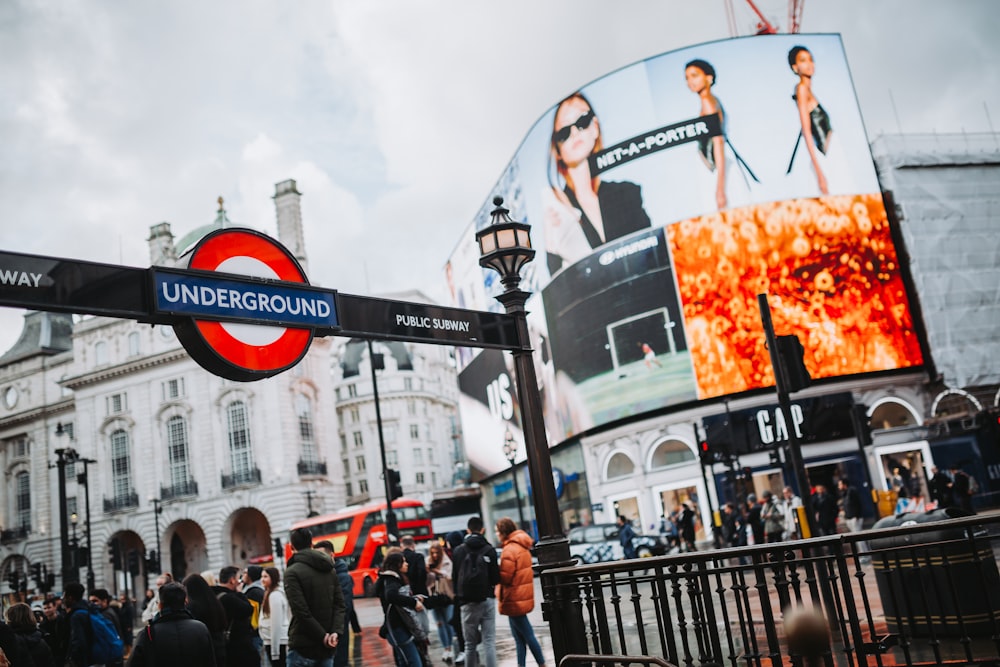 a crowd of people walking on a sidewalk next to a large billboard