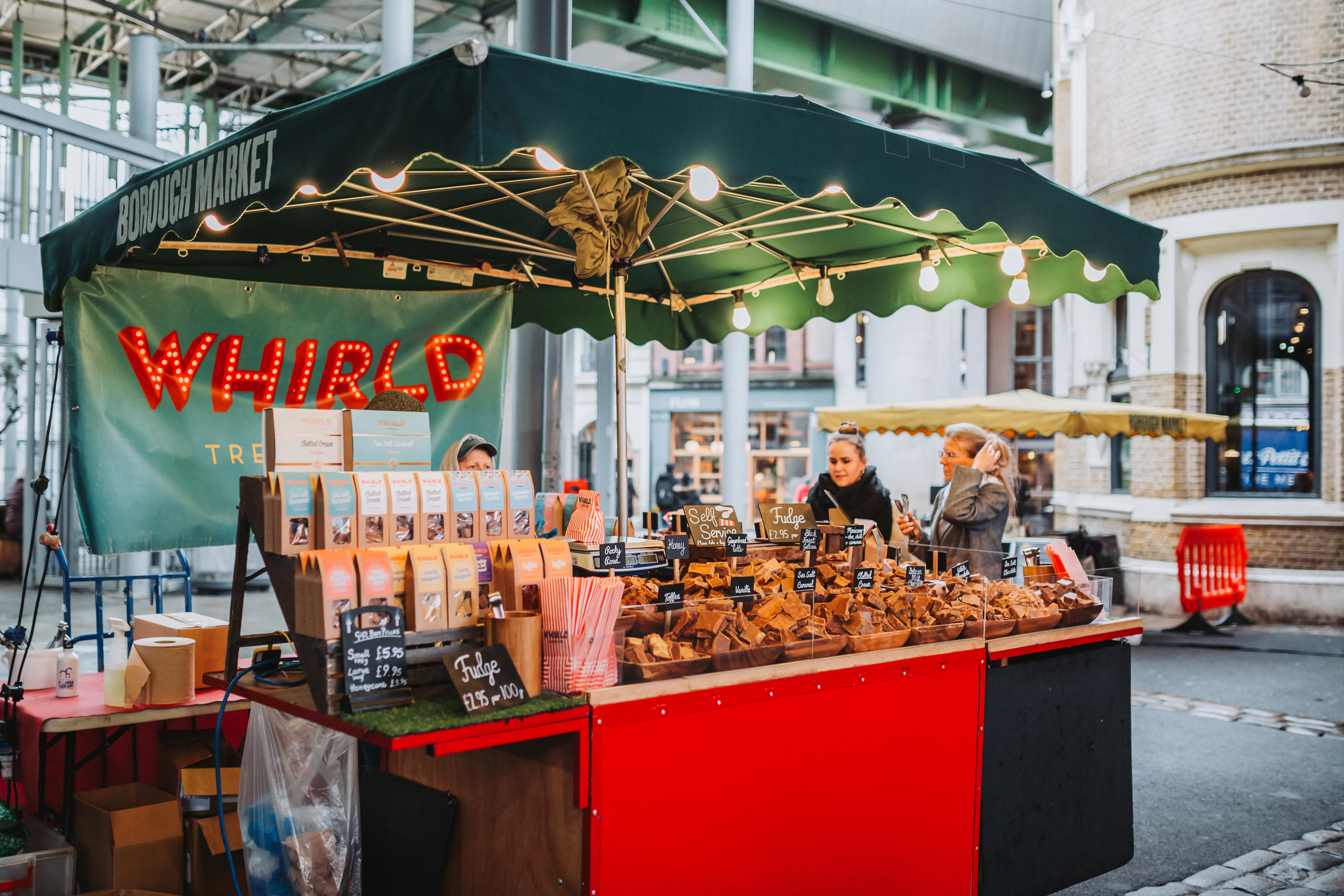 A food stall glowing with string lights and trays of prepared food at Borough Market.