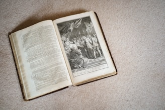 An open book is placed on a textured surface, displaying detailed text on the left page and an intricate black and white illustration on the right. The illustration features a historical or religious scene with several figures in classical attire, possibly depicting a significant event or story.
