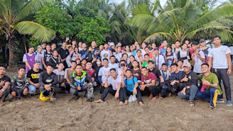 A friendly group photo of the Tata Shelly Beach team standing on the sandy shore with the ocean in the background.