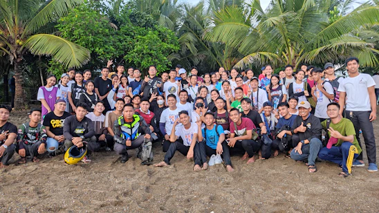 A friendly group photo of the Tata Shelly Beach team standing on the sandy shore with the ocean in the background.