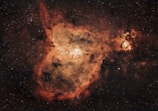A vast cosmic nebula with swirling clouds of dust and gas, showcasing a vibrant array of colors among the stars. The central area is a bright, densely packed region surrounded by darker, intricate filaments.
