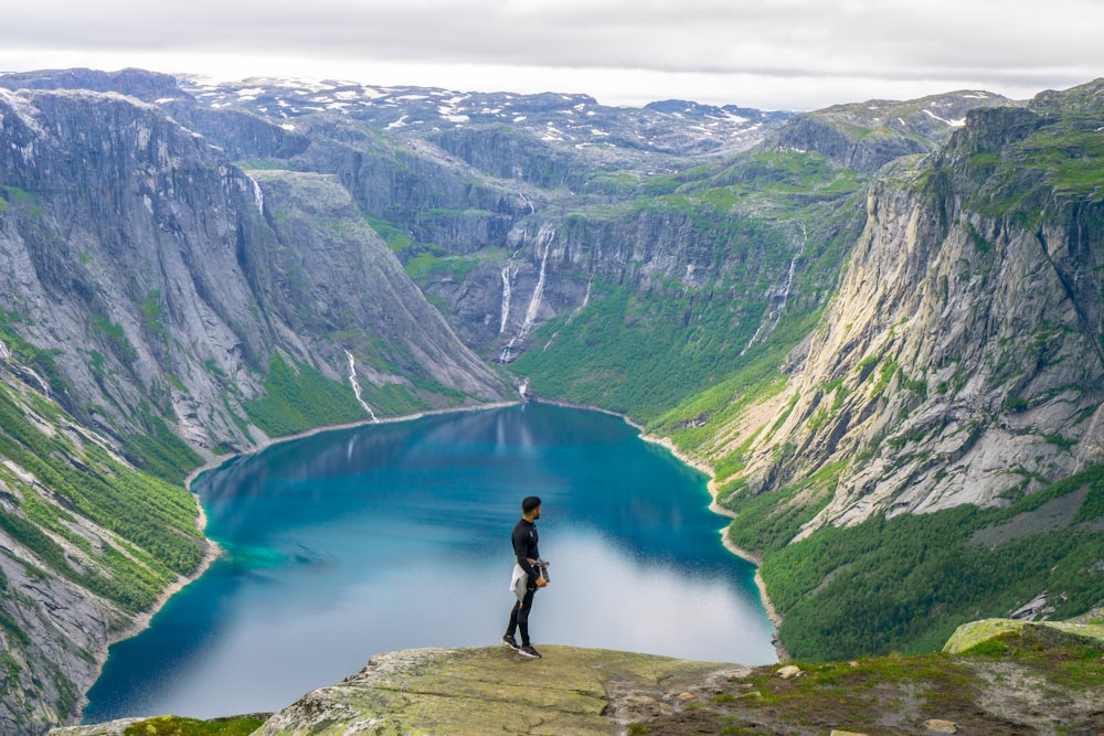 a man standing on a rock above a lake surrounded by mountains