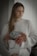 A person wearing a white knitted sweater is holding a white Chanel shopping bag filled with colorful hydrangea flowers, including shades of pink, mauve, and hints of purple. They have long, light brown hair and appear to be indoors with soft, natural lighting.