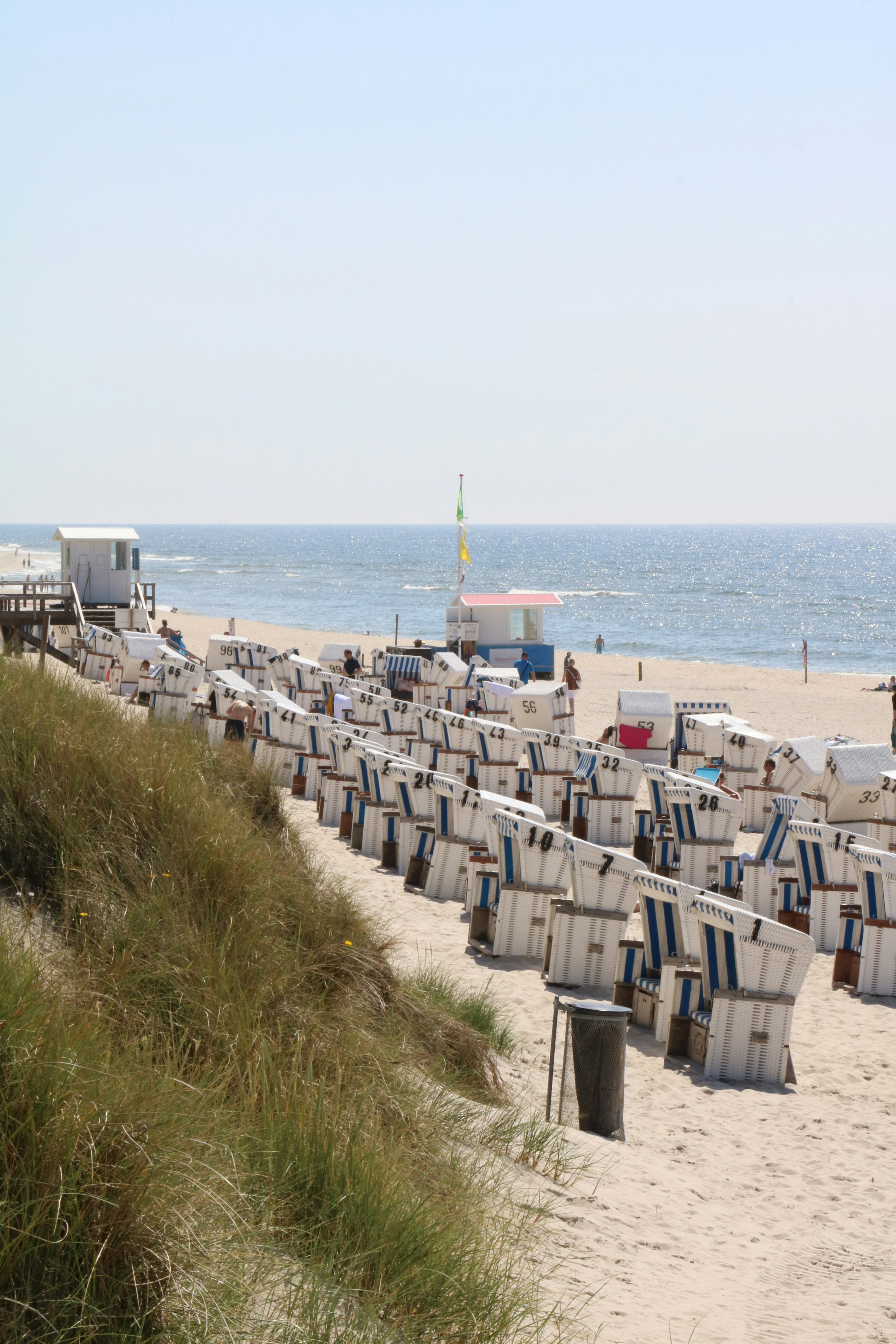 Row of blue and white striped beach chairs under large umbrellas on white sand beach facing ocean
