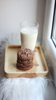 a cookie on a cutting board next to a glass of milk