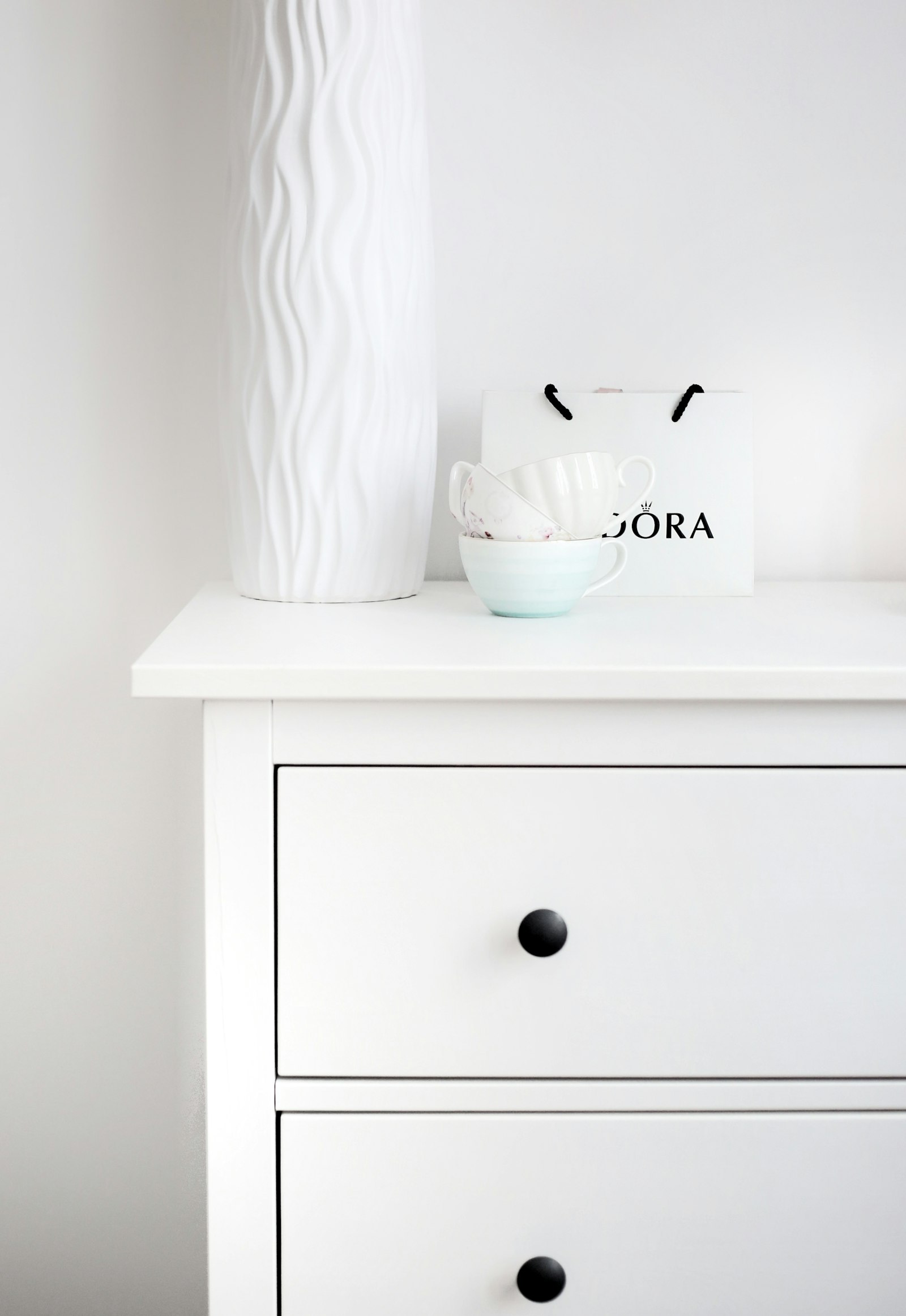 A white dresser with black knobs against a white wall