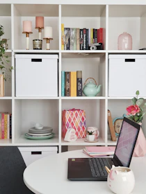 a white table with a laptop and a white shelf with books