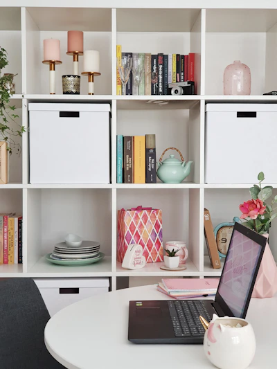 a white table with a laptop and a white shelf with books