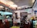A cozy cafe interior with wooden counters and decorative shelves. There are various action figures and trinkets displayed above the counter. A staff member is preparing drinks behind the counter, surrounded by coffee-making equipment. Menus with Korean writing are visible, featuring drink options. The ambiance is warm and eclectic, with touches of vintage decor.