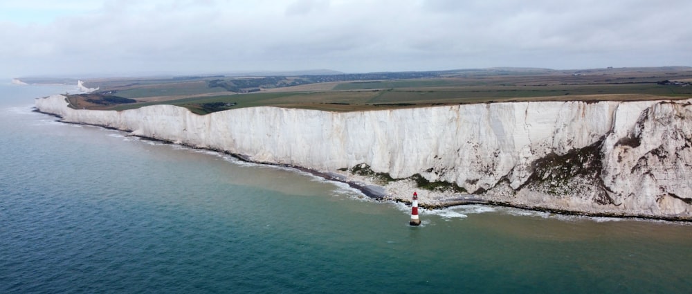 a body of water with a rocky cliff and a lighthouse with White Cliffs of Dover in the background
