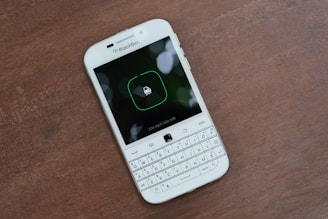 A white BlackBerry smartphone is placed on a wooden surface. The phone has a physical QWERTY keyboard and its screen displays a lock icon with Vietnamese text underneath.