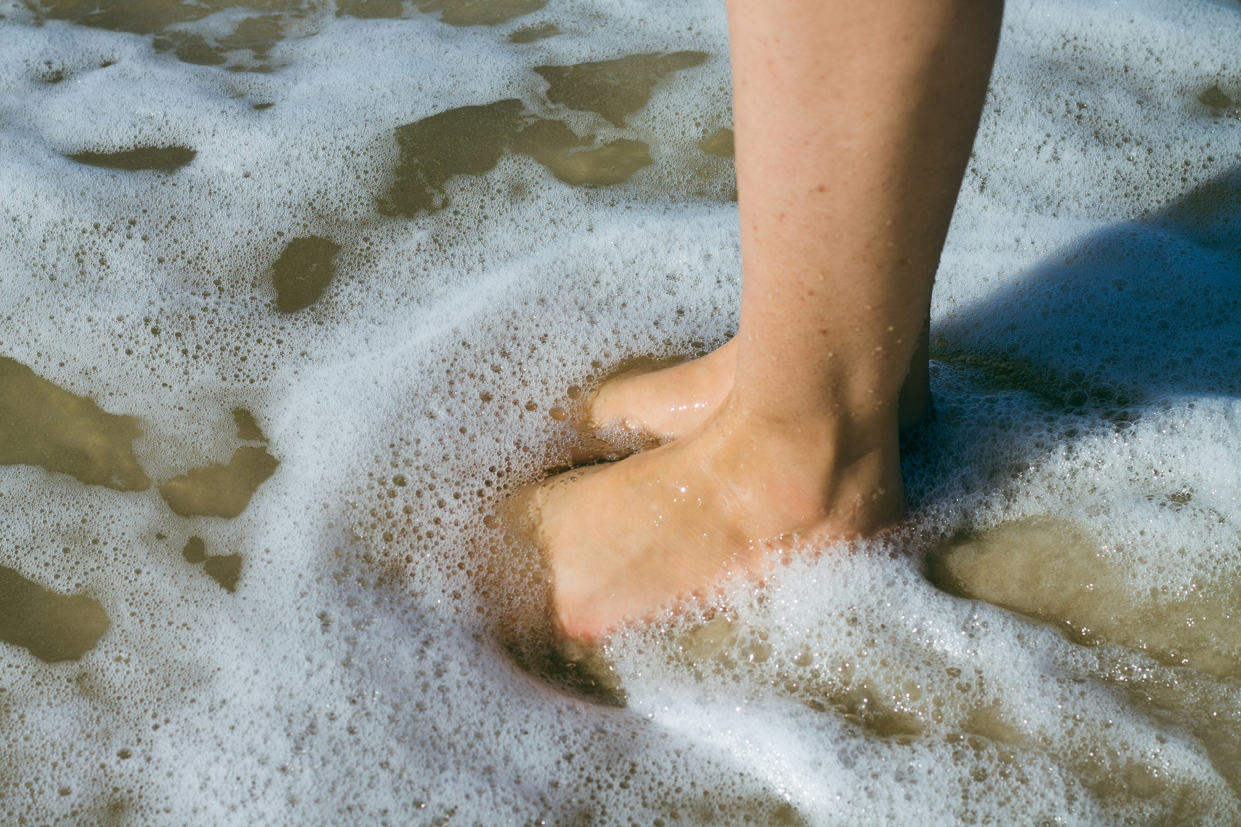 Närbild av en persons fötter i sanden med mjuka vågor som tvättar över dem.