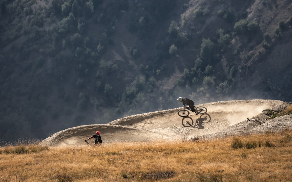 a couple of people riding bikes on a dirt road with trees in the background