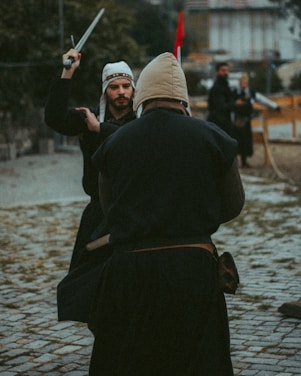 Medieval sword fight reenactment in an outdoor arena with spectators watching.