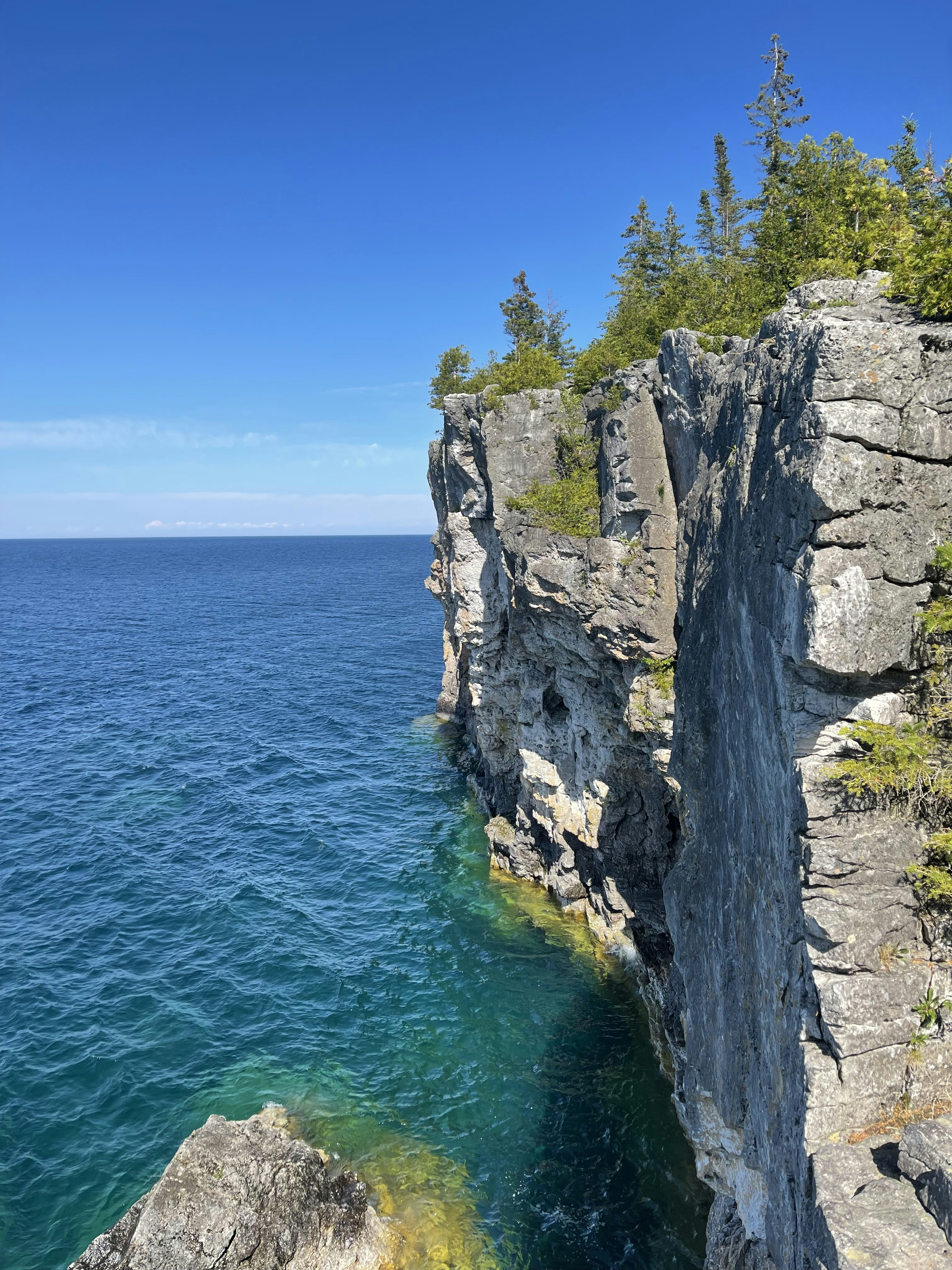 a cliff side with a body of water below with Bruce Peninsula National Park in the background