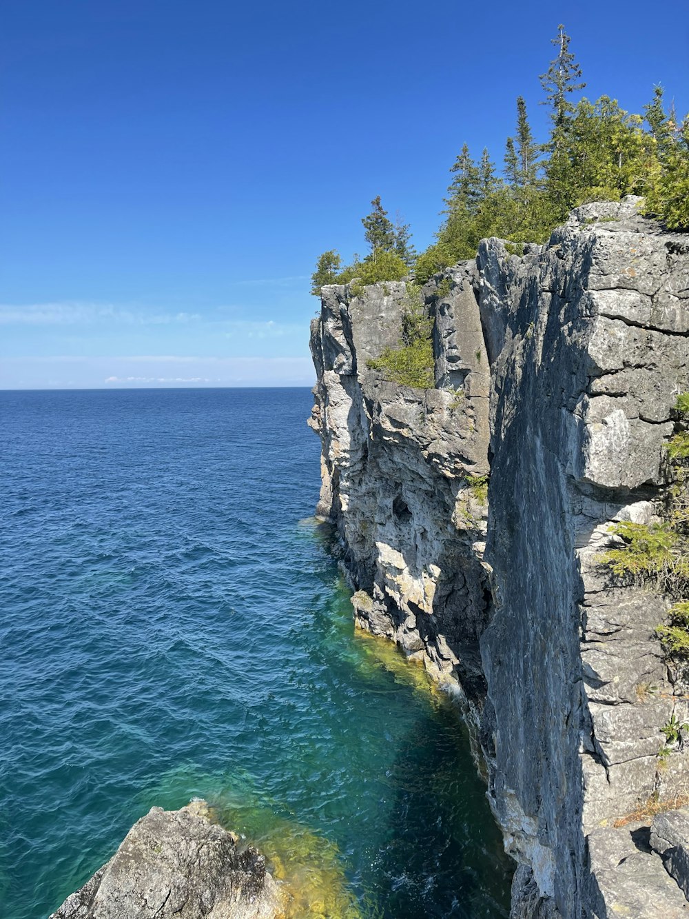 a cliff side with a body of water below with Bruce Peninsula National Park in the background