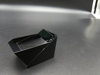 A sleek modern 3D black and grey geometric shape with ultra-realistic textures reflecting light subtly.