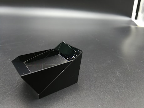 A sleek modern 3D black and grey geometric shape with ultra-realistic textures reflecting light subtly.