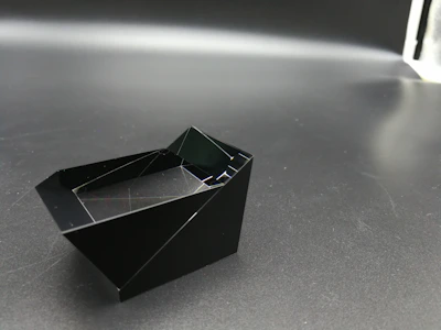 Close-up of a sleek black 3D printed geometric sculpture with smooth surfaces and sharp edges on a dark background