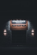 A dimly lit sign for 'Gahan House Harbourview' is displayed on a wooden background. It features sections labeled 'Restaurant,' 'Oyster Bar,' and 'Brewery,' with light fixtures on each side, creating a cozy and inviting atmosphere.