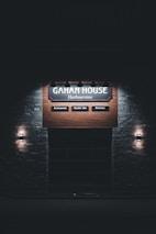A dimly lit sign for 'Gahan House Harbourview' is displayed on a wooden background. It features sections labeled 'Restaurant,' 'Oyster Bar,' and 'Brewery,' with light fixtures on each side, creating a cozy and inviting atmosphere.