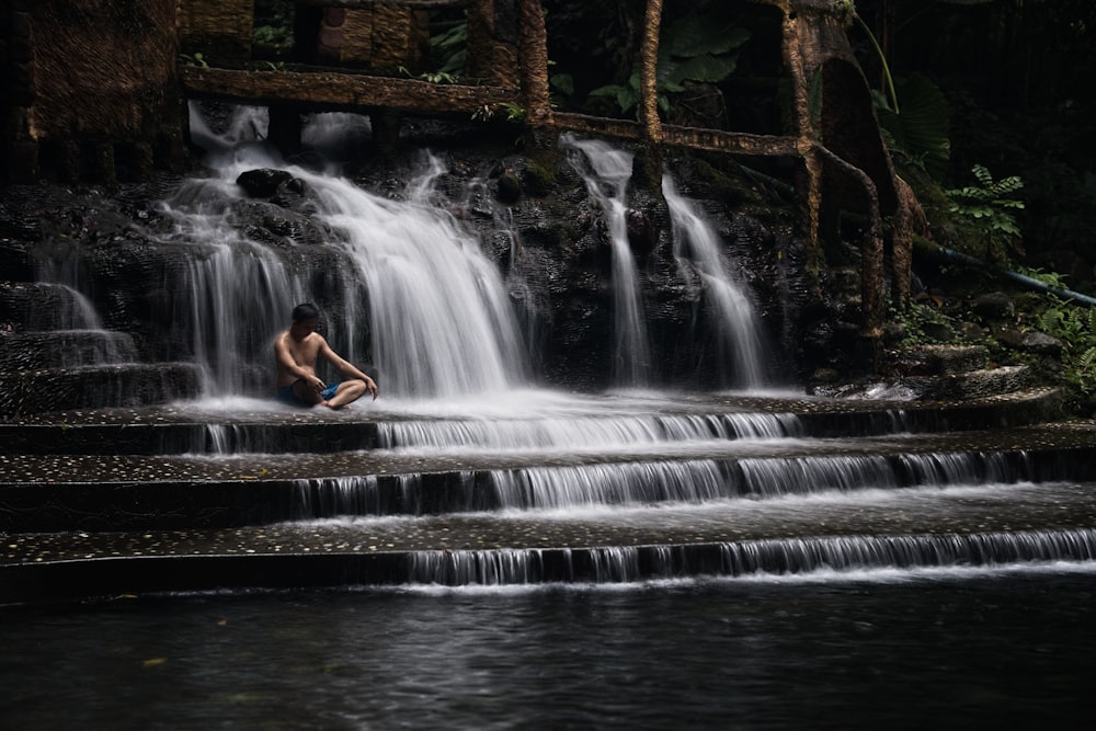 uma pessoa sentada em uma rocha na frente de uma cachoeira