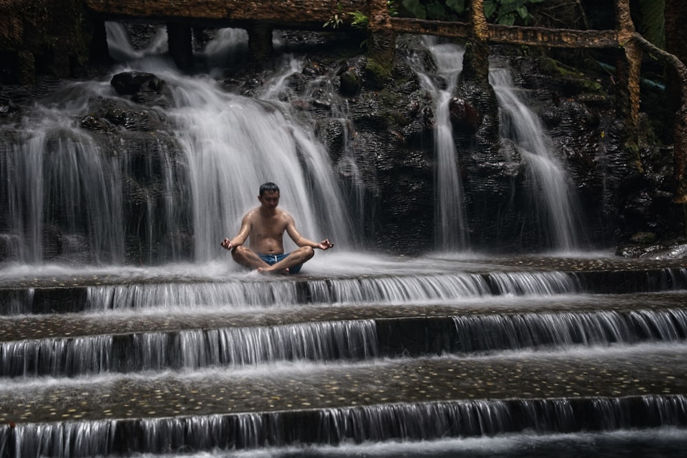 a man sitting on a rock in front of a waterfall