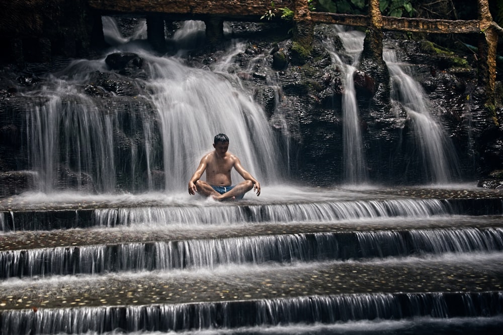 a man sitting on a rock in front of a waterfall