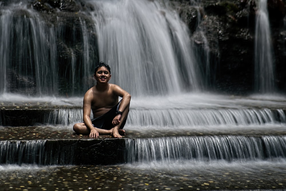 a man sitting on a rock in front of a waterfall