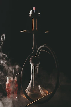 Close-up of a sleek black and gold hookah with swirling aromatic smoke against a dark, elegant background.
