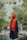a person wearing a black robe and red head covering standing in front of a pond with trees and