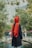 a person wearing a black robe and red head covering standing in front of a pond with trees and